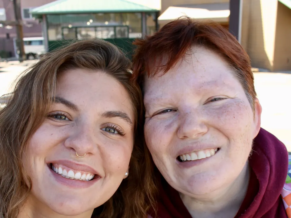 Two people smiling cheek to cheek in a sunny outdoor selfie.